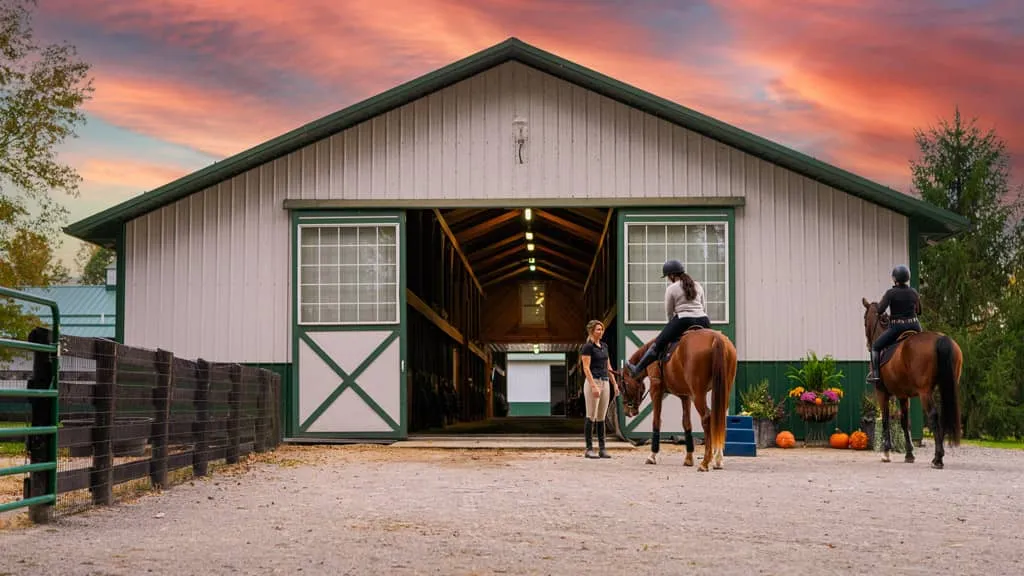 Riders on horses outside a barn at Still Water Farm with a sunset in the sky
